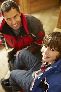 Father Helping Son To Put On Warm Outdoor Clothes And Boots