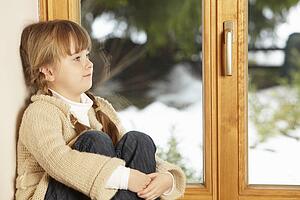 Young Girl Sitting On Window Ledge Looking At Snowy View