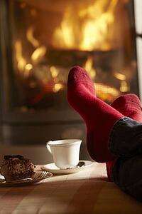Close Up Of Mans Feet Relaxing By Cosy Log Fire With Tea And Cake