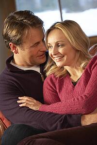 Middle Aged Couple Chatting On Sofa In Chalet With Winter View