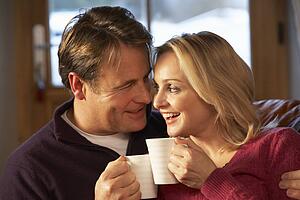 Middle Aged Couple Sitting On Sofa With Hot Drinks