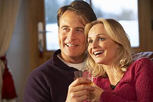 Middle Aged Couple Sitting On Sofa With Glasses Of Whisky Watching TV