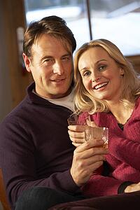 Middle Aged Couple Sitting On Sofa With Glasses Of Whisky