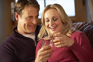 Middle Aged Couple Sitting On Sofa With Glasses Of Whisky