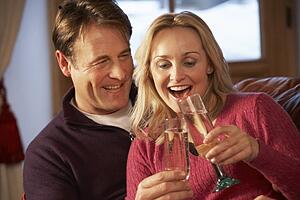 Middle Aged Couple Sitting On Sofa With Glasses Of Champagne