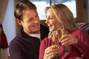 Middle Aged Couple Sitting On Sofa With Glasses Of Champagne