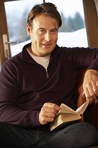 Middle Aged Man Relaxing With Book Sitting On Sofa