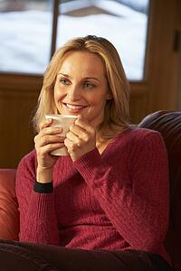 Middle Aged Woman Relaxing With Hot Drink On Sofa Watching TV