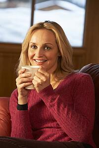 Middle Aged Woman Relaxing With Hot Drink On Sofa Watching TV