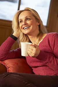 Middle Aged Woman Relaxing With Hot Drink On Sofa Watching TV