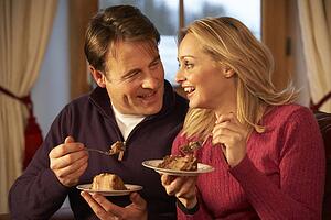 Couple Enjoying Slice Of Cake Sitting On Sofa
