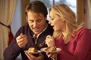 Couple Enjoying Slice Of Cake Sitting On Sofa