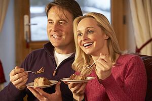 Couple Enjoying Slice Of Cake Sitting On Sofa Watching TV