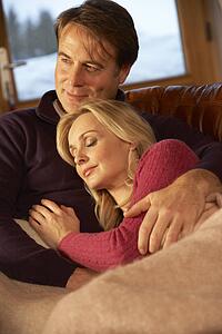 Middle Aged Couple Relaxing On Sofa In Chalet With Winter View