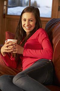Teenage Girl Relaxing On Sofa With Hot Drink