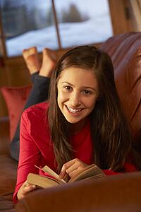 Teenage Girl Relaxing On Sofa Reading Book