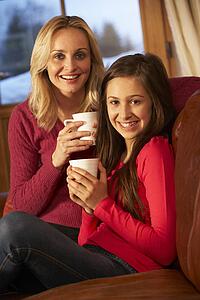 Portrait Of Mother And Daughter Relaxing On Sofa Together With Hot Drink