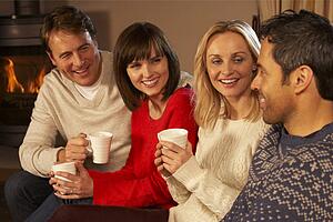 Group Of Middle Aged Couples Sitting On Sofa With Hot Drinks Talking