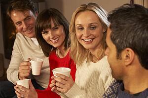 Group Of Middle Aged Couples Sitting On Sofa With Hot Drinks Talking