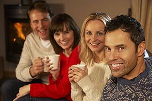 Group Of Middle Aged Couples Sitting On Sofa With Hot Drinks Talking