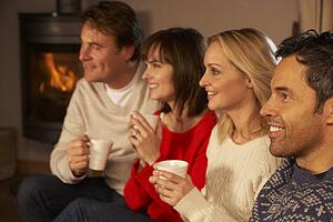 Group Of Middle Aged Couples Sitting On Sofa With Hot Drinks Watching TV