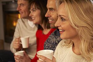Group Of Middle Aged Couples Sitting On Sofa With Hot Drinks Watching TV
