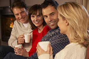 Group Of Middle Aged Couples Sitting On Sofa With Hot Drinks Talking