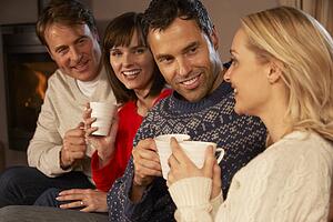 Group Of Middle Aged Couples Sitting On Sofa With Hot Drinks Talking