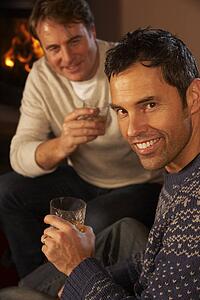 Two Middle Aged Men Relaxing Sitting On Sofa Drinking Whisky