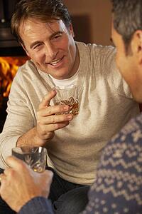 Two Middle Aged Men Relaxing Sitting On Sofa Drinking Whisky