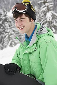 Teenage Boy With Snowboard On Ski Holiday In Mountains