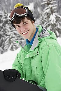 Teenage Boy With Snowboard On Ski Holiday In Mountains