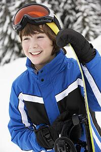Young Boy With Snowboard On Ski Holiday In Mountains