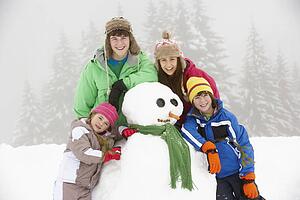 Group Of Children Building Snowman On Ski Holiday In Mountains