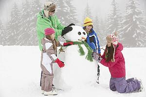 Group Of Children Building Snowman On Ski Holiday In Mountains