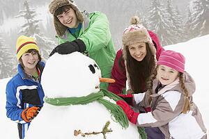 Group Of Children Building Snowman On Ski Holiday In Mountains