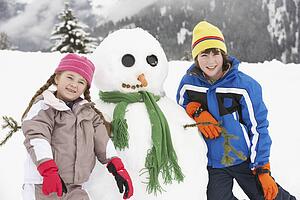 Two Young Children Building Snowman On Ski Holiday In Mountains