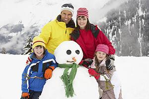 Family Building Snowman On Ski Holiday In Mountains