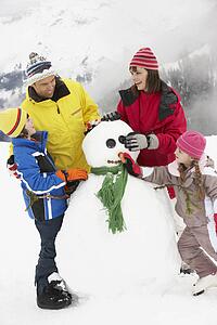 Family Building Snowman On Ski Holiday In Mountains
