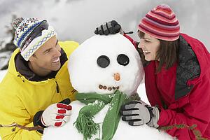Middle Aged Couple Building Snowman On Ski Holiday In Mountains