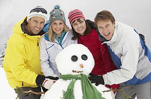 Group Of Friends Building Snowman On Ski Holiday In Mountains