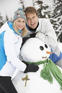 Middle Aged Couple Building Snowman On Ski Holiday In Mountains
