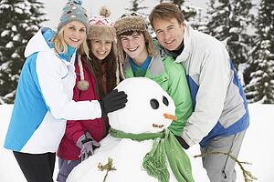 Teenage Family Building Snowman On Ski Holiday In Mountains