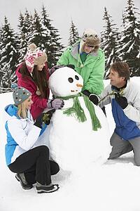 Teenage Family Building Snowman On Ski Holiday In Mountains