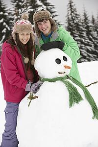 Two Teenagers Building Snowman On Ski Holiday In Mountains