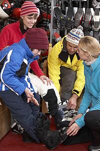Sales Assistant Helping Family To Try On Ski Boots In Hire Shop