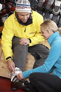 Sales Assistant Helping Man To Try On Ski Boots In Hire Shop