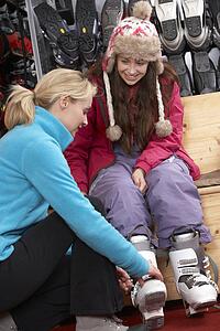 Sales Assistant Helping Teenage Girl To Try On Ski Boots In Hire Shop