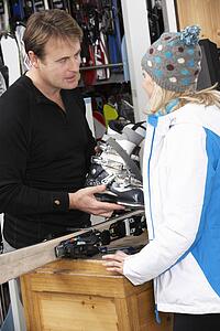 Sales Assistant Helping Advising Female Customer On Ski Boots In Hire Shop