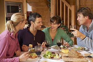 Group Of Friends Enjoying Meal In Alpine Chalet Together